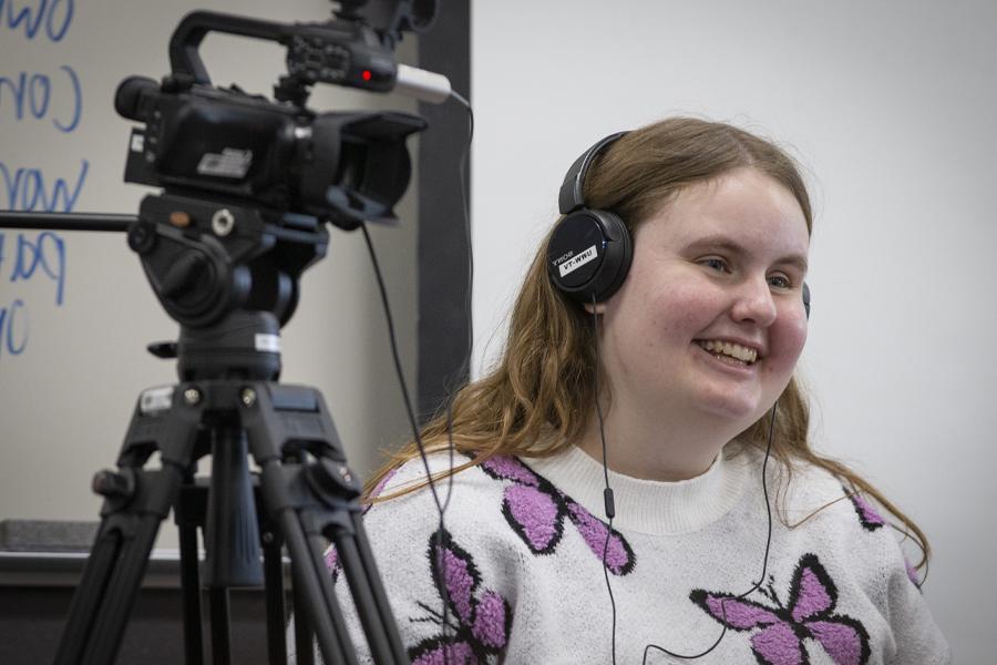 Warhawk Angie Angie Carchesi wears a headset and stands next to a video camera.